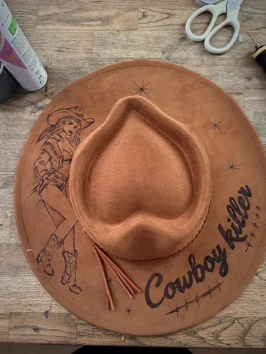 Tan hat with a pin-up cowgirl and “Cowboy Killer” burned into the brim