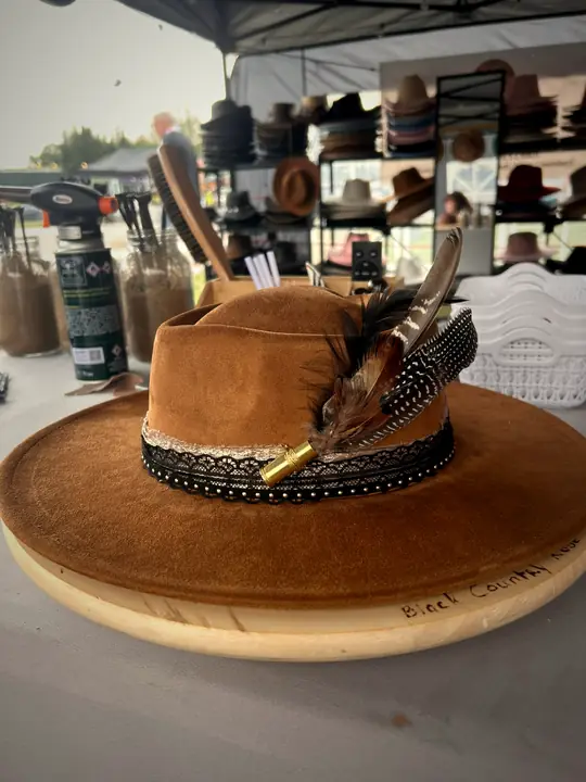 Tan wide-brim hat with black lace band and feather bullet pick