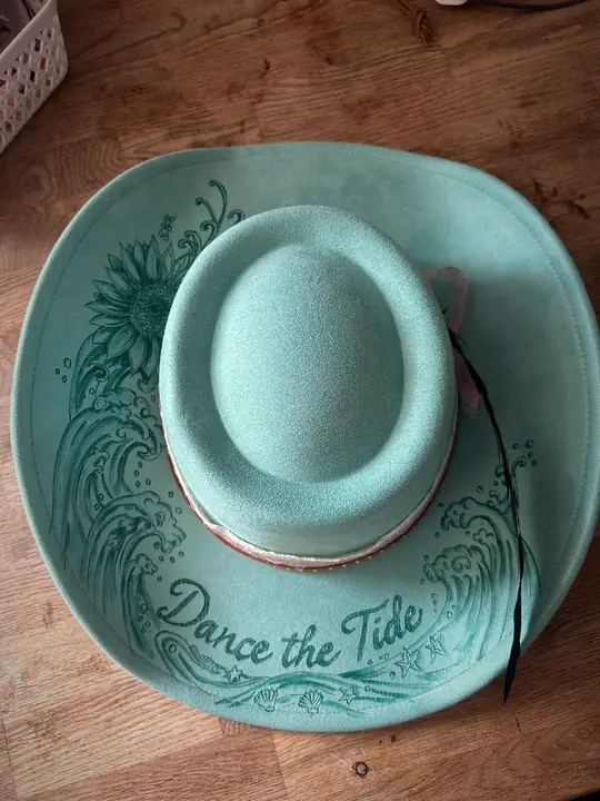 Turquoise hat with “Dance the Tide”, waves and a sunflower burned into the brim